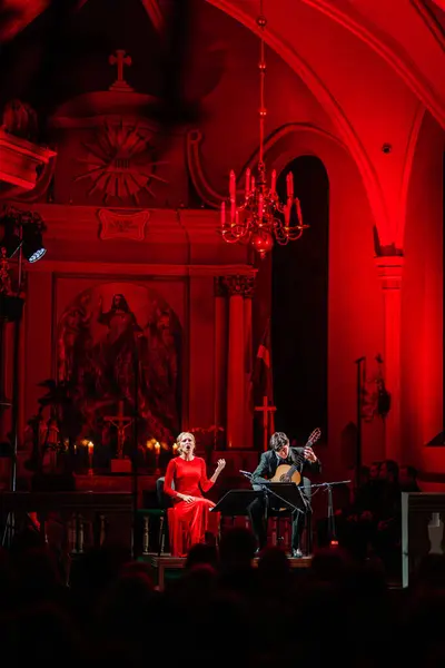 2024年1月7日 ラトビア セントサイモン教会 赤いドレスの女性が歌い 背景に祭壇画を描いた教会のコンサートでギターを弾く男 — ストック写真