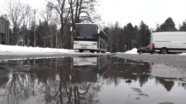 2024年2月13日 拉脱维亚西古尔达市 一辆在湿路上行驶的公共汽车 车上有雪堆和水坑中的倒影 还有背景中的树木 — 图库视频影像