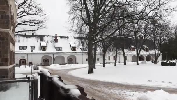 ラトビアのシグルダ 2024年2月13日 裸の木と雪に囲まれたアーチ型の入り口と雪に覆われた屋根を持つ歴史的な白い建物 — ストック動画