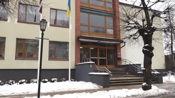 セシス ラトビア 2024年2月13日 背景にある建物と旗を持つ雪の通りを移動する車 — ストック動画