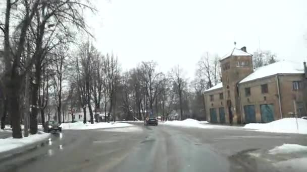 セシス ラトビア 2024年2月13日 道路標識 その隣に雪が積まれたレンガ造りの建物が裸の木に囲まれています 車から撮影 — ストック動画
