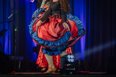 Valmiera, Letonya - 15 Şubat 2024 - Geleneksel çingene konserinde etek kıvıran kadın dansçıların yakın çekimi, arka planda canlı mavi sahne ışıklandırması