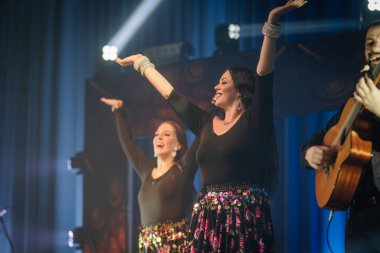 Valmiera, Letonya - 15 Şubat 2024 - İki neşeli kadın kollarını kaldırıyor, büyük ihtimalle şarkı söylüyor ya da dans ediyorlar, canlı geleneksel çingene konserinde gitar çalan bir adamla.
