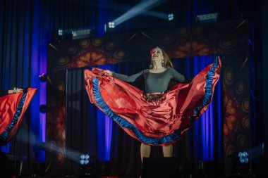Valmiera, Letonya - 15 Şubat 2024 - Kırmızı etekli neşeli bir bayan dansçı çingene geleneksel konserinde mavi ve mor sahne ışıklarıyla sahnede sahne alıyor.
