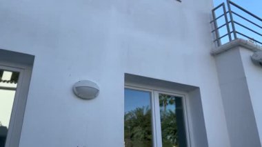 Sotogrande, İspanya - 22 Ocak 2024 - Yuvarlak duvarlı bir binanın dış duvarı, palmiye ağaçlarını yansıtan büyük cam kapı ve açık mavi gökyüzü.
