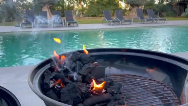 2024年1月22日 西班牙索托格朗德 一个燃烧着火焰的烤肉烤架 在一个游泳池前 后面有躺椅和树木 — 图库视频影像
