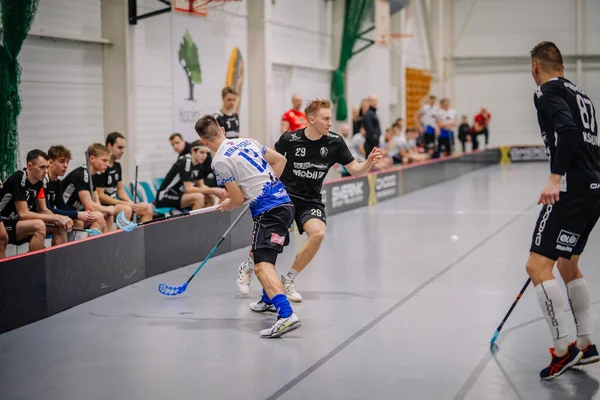 Valmiera, Letonya - 17 Şubat 2024 - Bir maçta iki florbol oyuncusu, biri siyah ve diğeri beyazlı, takım arkadaşları ile birlikte yedek kulübesinde maç yapıyorlar..