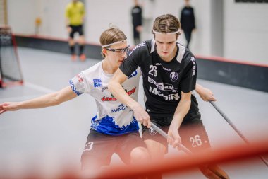 Valmiera, Letonya - 17 Şubat 2024 - Top için düelloda iki florbol oyuncusu, beyazlı bir kadın ve siyahlı bir adam, ikisi de oyuna odaklanmış..