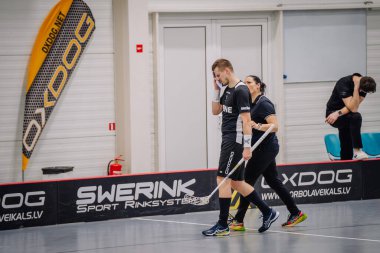 Valmiera, Letonya - 17 Şubat 2024 - Siyah üniformalı iki kişi ringin kenarında yürüyor, biri yüzünü örtüyor, üzgün veya yorgun görünüyor.