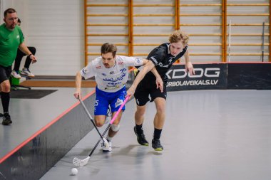 Valmiera, Letonya - 17 Şubat 2024 - Spor salonunda iki erkek oyuncu arka planda bir hakem ile bir florbol maçında yarışıyor..