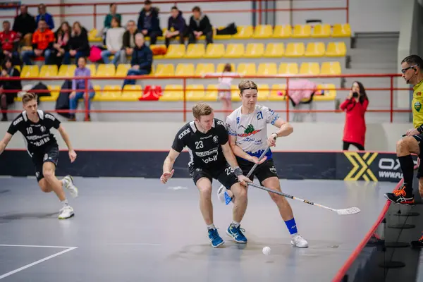 Valmiera, Letonya - 17 Şubat 2024 - iki florbol oyuncusu, biri siyah ve biri beyaz, bir maç sırasında hareket halindeler, arka planda seyirciler var.