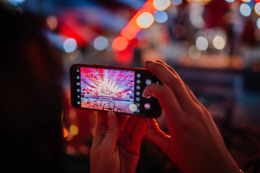 Riga, Letonya - 16 Şubat 2024 - Bir akıllı telefon tutan eller ekranda renkli ışıklandırmalı bir sahneyi çekiyor.