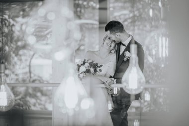 Riga, Letonya - 20 Ocak 2024 - Bir gelin ve damat birbirine yakın, etrafı bulanık ışıklarla çevrili, damat öne eğilmiş.