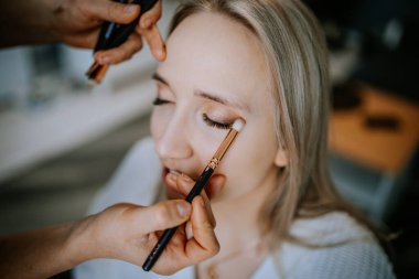 Riga, Letonya - 20 Ocak 2024 - Makyaj sanatçısı bir kadının göz kapağına göz farı sürüyor.