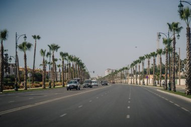 Agadir, Fas - 25 Şubat 2024 - Palmiye ağaçları ve sokak lambalarıyla kaplı geniş bir bulvar, arabalar çalışıyor ve açık mavi gökyüzü.