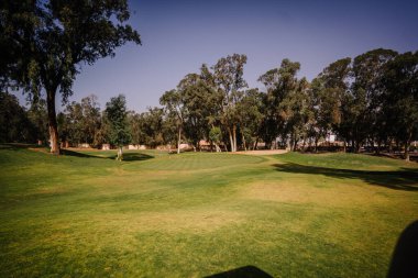 Agadir, Fas - 25 Şubat 2024 - Berrak bir gökyüzü altında yemyeşil, bir kum sığınağı ve ağaçlarla dolu sakin bir golf sahası.