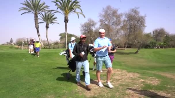 アガディール モロッコ 2024年2月27日 青いシャツのゴルファーは コースの背景にある他のゴルファーやバッグと赤いキャップのキャディにお金を渡しています — ストック動画