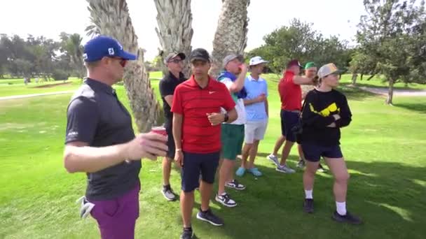 摩洛哥阿加德德 2024年2月27日 一群穿着各种装束的高尔夫球手站在球场上 其中一些人拿着饮料和智能手机 背景是棕榈树 — 图库视频影像