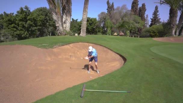 摩洛哥阿加德德 2024年2月27日 一名身穿蓝色衬衫的高尔夫球手在高尔夫球场的沙坑里挥动一根棍棒 后面是树木和绿草 — 图库视频影像
