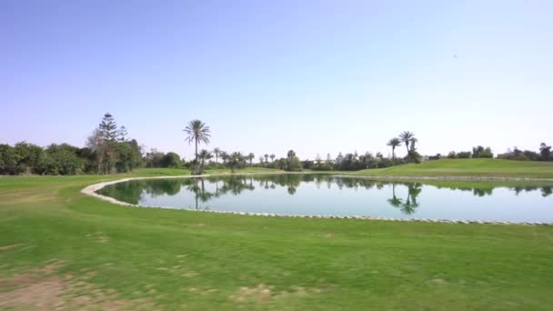 アガディール モロッコ 2024年2月27日 明るい青空の下の周囲の木々を反映したウォーターハザードのゴルフコースビュー 緑のフェアウェイ — ストック動画