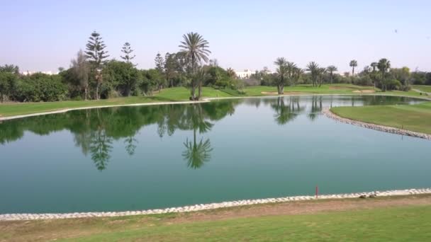 アガディール モロッコ 2024年2月27日 穏やかな水の危険は 緑豊かで澄んだ青空と晴れたゴルフコースでヤシの木々と空を反映しています — ストック動画
