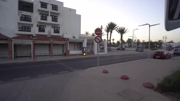 アガディール モロッコ 2024年2月27日 アラビア語 ヤシの木 閉店店店で赤い停留所サインを示す駐車場を残すバスの窓からのストリートビュー — ストック動画
