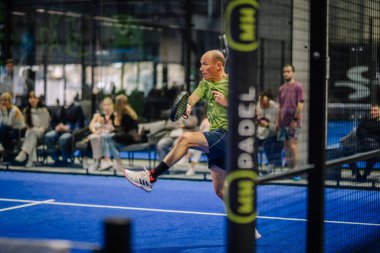 Riga, Letonya - 3 Mart 2024 - Yaşlı bir adam orta sıçrayışta iç sahadaki bir topa vuruyor ve seyirciler yumuşak odaklı arka planda görülüyor.