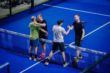 Riga, Letonya - 3 Mart 2024 - Oyuncular Padel kortu üzerinden dostça bir takasa giriştiler; ikisi el sıkışıyorlar, diğeri ise iyi bir sportmenlik sergiliyor..