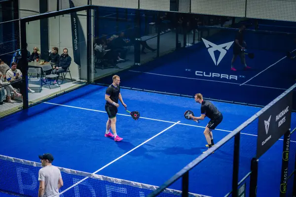 Riga, Letonya - 3 Mart 2024 - İki erkek oyuncu CUPRA markalaşması ile kapalı bir mavi padel sahaya odaklanmış durumda.