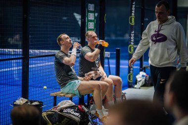 Riga, Letonya - 3 Mart 2024 - Bir maçta iki Padel oyuncusu su içerken, bir koç ya da bir oyuncu beklemede.