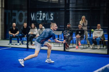Riga, Letonya - 3 Mart 2024 - Hamle pozisyonu almış bir erkek oyuncu arka planda seyircilerle topa vurmaya hazır.