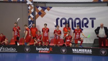 Valmiera, Letonya, 10 Mart 2024 - kırmızı üniformalı bir spor takımı oturmakta ve yedek kulübesinde duruyor.