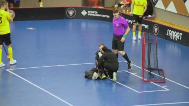 Valmiera, Letonya, 10 Mart 2024 - Bir spor sahasında, bir sağlık personeli yaralı bir kaleciye yardımcı olmak için koşar..