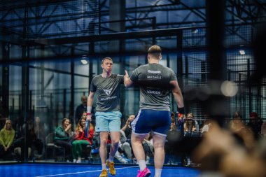 Riga, Letonya - 3 Mart 2024 - İki Padel oyuncusu sahada, biri kameraya dönük, diğeri ise arkası dönük.