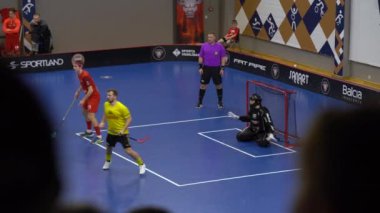 Valmiera, Letonya - 10 Mart 2024 - İç saha spor sahasında, hareket halindeki florbol oyuncuları siyah kıyafetli kalecinin etrafını sarıyorlar, maç devam ediyor ve bir hakem yakınlarda.