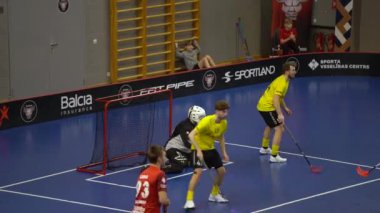 Valmiera, Letonya - 10 Mart 2024 - Siyah formalı kaleci kalede, kırmızı maçın oyuncuları sarıya karşı. Floorball oyunu