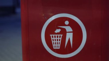 Valmiera, Letonya - 10 Mart 2024 - Kırmızı arka planda bir resim, çöp kutusuna çöp atan bir figürün çöp öğütücüsünü sembolize ettiğini gösteriyor.