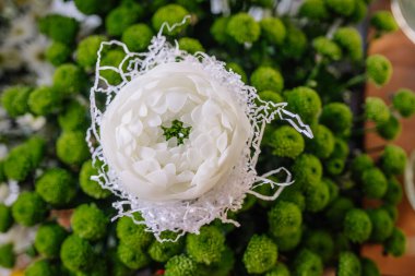 Valmiera, Letonya - 7 Mart 2024 - Arkaplanda yeşil küresel çiçekler bulunan, kağıt parçalarıyla çevrili, çiçek şeklinde beyaz bir mum manzarası.