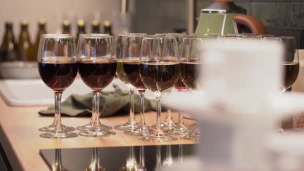 ワイングラスは赤と白のワインを含む反射面に配置され バーやキッチンセッティングを示唆するぼやけた背景があります — ストック動画