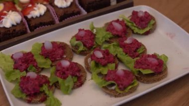 Kırmızı pancar soslu açık yüzlü sandviç tepsisi, marul ve soğanla süslenmiş, yanında krem şantili çikolatalı brownie..