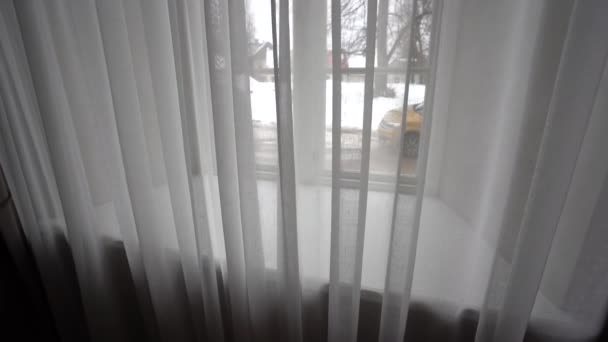 セシス ラトビア 2024年2月14日 窓の白いカーテンを通しての景色 雪の街路シーンと外の黄色い車を垣間見る — ストック動画