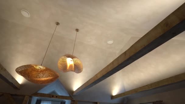 露出された木のビームが付いている質感の天井から掛かる2つの編まれたペンダント ライト — ストック動画