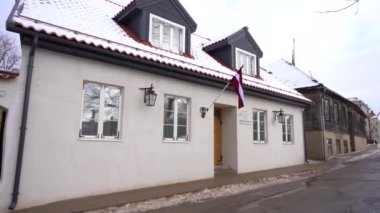 Cesis, Letonya - 14 Şubat 2024 - karla kaplı terasotta çatısı, beyaz pencereleri, feneri ve Letonya bayrağı olan iki katlı beyaz bir bina.