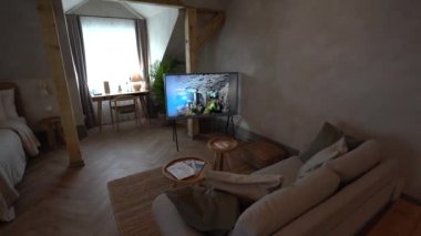Cesis, Letonya - 14 Şubat 2024 - Yatağı olan rahat bir stüdyo daire, TV sergisi, lambalı bir çalışma masası, yastıklı bir kanepe ve yuvarlak ahşap bir masa.