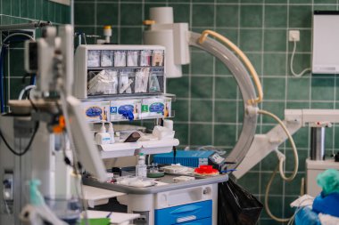 Valmiera, Letonya - 20 Mart 2024 - Tıbbi ekipman ve malzemeler, arka planda C-kolu floroskobu ve cerrahi masası olan bir cerrahi odasında bir el arabasında düzenlenir..