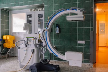 Valmiera, Latvia - March 20, 2024 - a Siemens Cios Fusion mobile C-arm X-ray machine in an operating room, with its curved arm and monitors, designed for surgical imaging. clipart