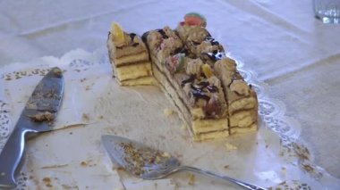 Katmanlı pastadan dilimler, krema ve çeşitli malzemeler bir pasta sunucusuyla birlikte masada bırakılır..