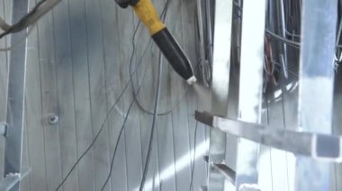 Valmiera, Letonya - 17 Mart 2024 - Arka planda kıvılcımlar ve kablolar olan metal yapıda sarı boya tabancası kullanan eldivenli elin yakın çekimi.