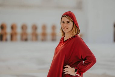 Dubai, Birleşik Arap Emirlikleri - 19 Ekim 2019 - Kırmızı tunik ve başörtülü kadın saçına dokunuyor, arka planda camiler bulanıklaşıyor