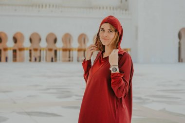 Dubai, Birleşik Arap Emirlikleri - 19 Ekim 2019 - Kırmızı tunik ve başörtülü kadın saçına dokunuyor, arka planda camiler bulanıklaşıyor